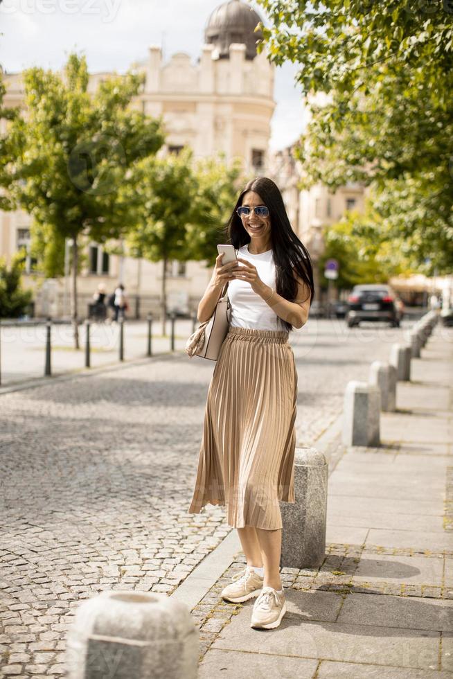 jonge vrouw met behulp van een mobiele telefoon tijdens het wandelen op straat foto