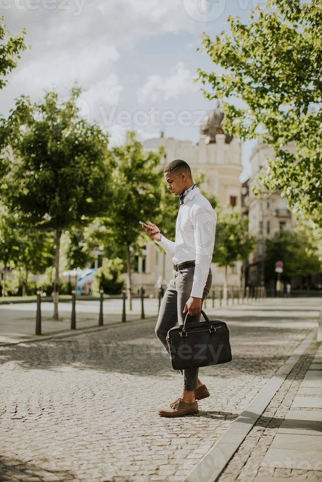 jonge Afro-Amerikaanse zakenman met behulp van een mobiele telefoon in een straat foto