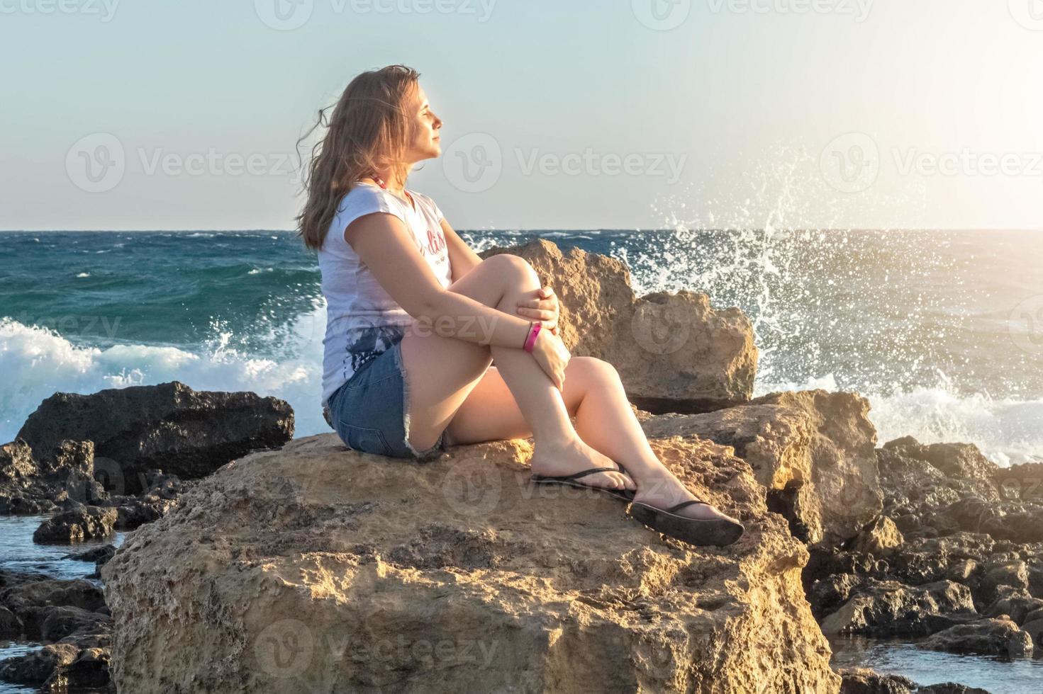 een jonge vrouw zit aan de kust van de Middellandse Zee bij zonsondergang foto