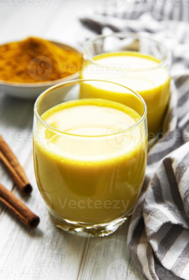 gele kurkuma latte-drank. gouden melk met kaneel, kurkuma, gember en honing op witte marmeren achtergrond. foto