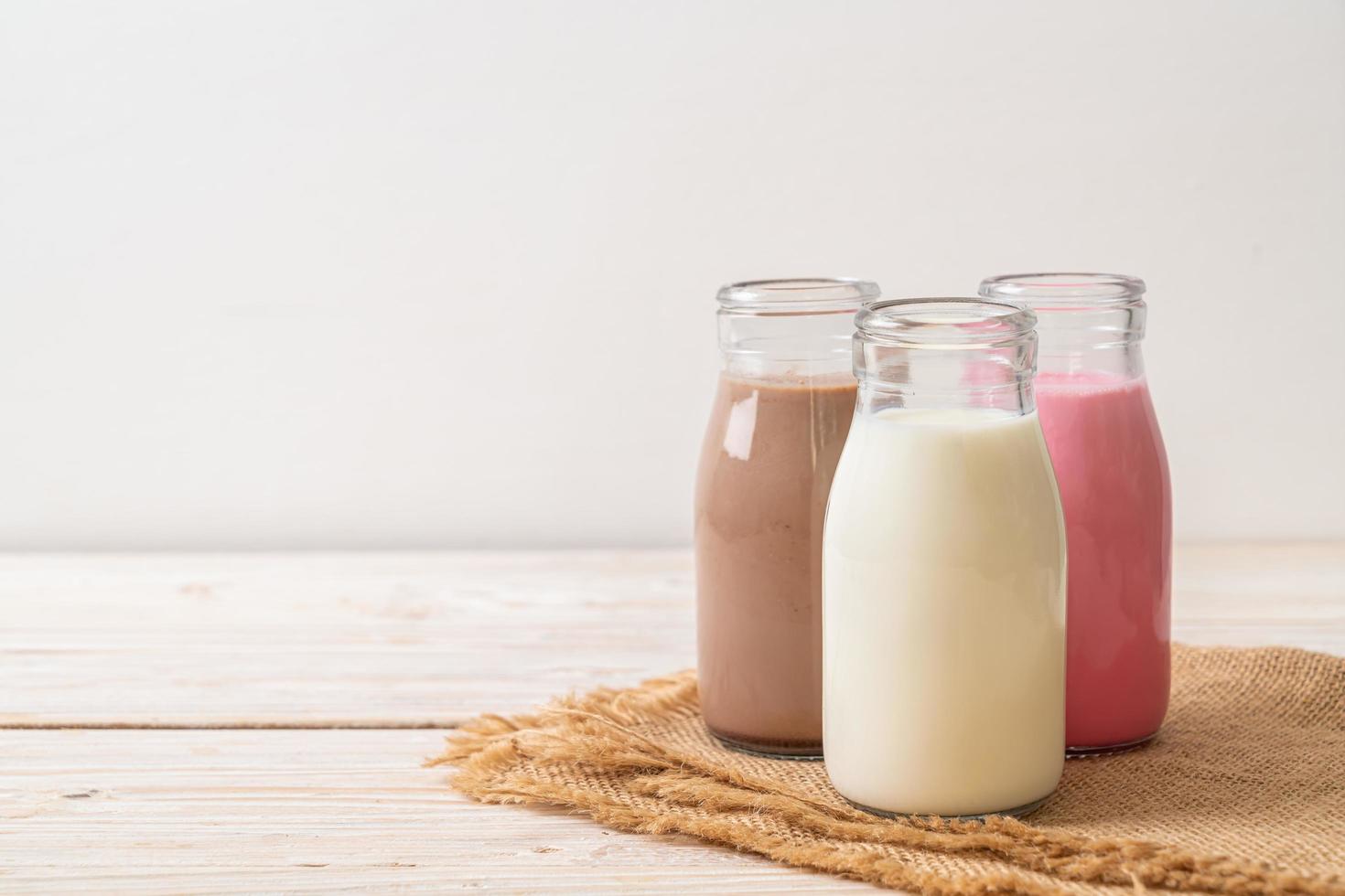 verzameling drankchocolademelk, roze melk en verse melk in fles op houten tafel foto