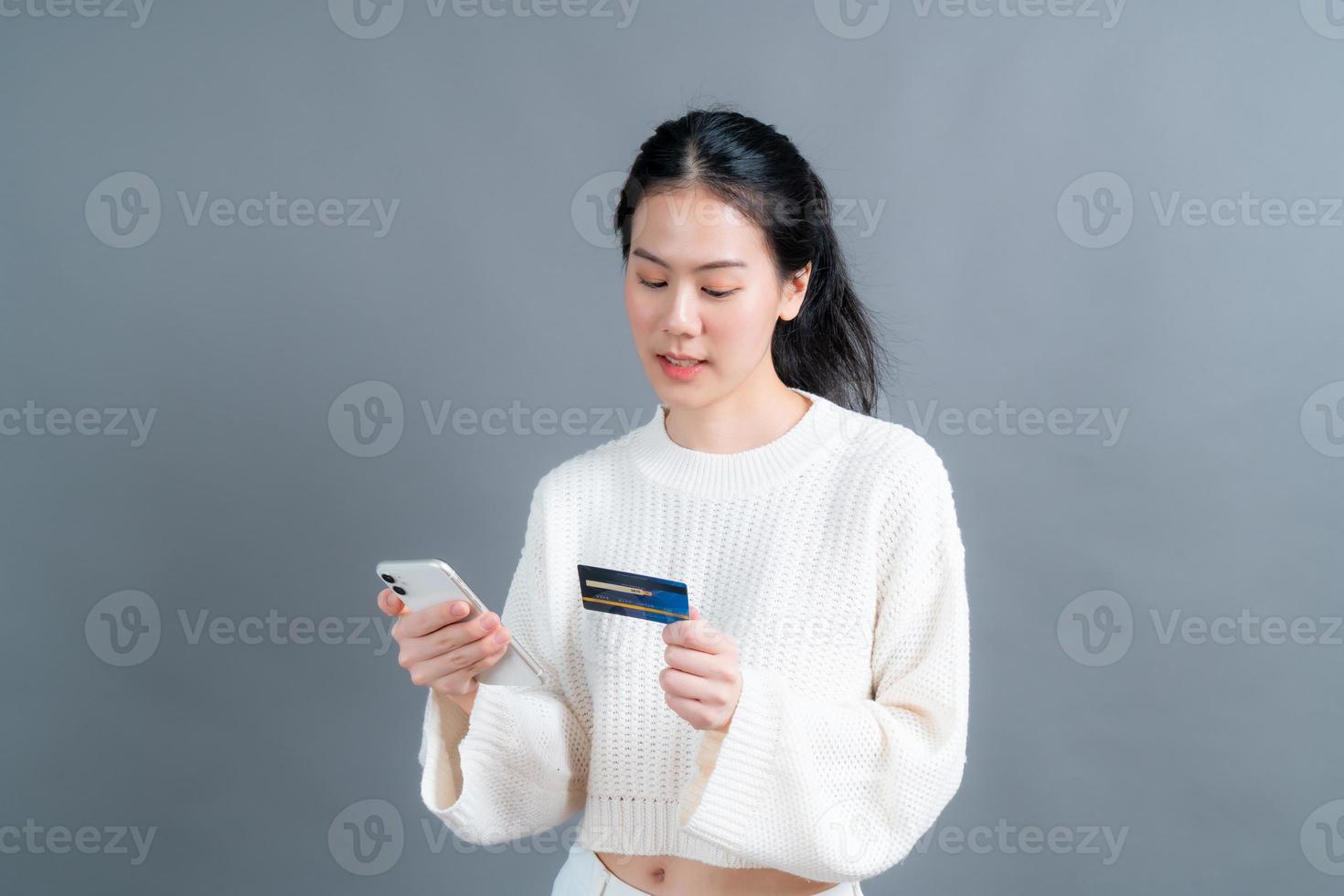 jong Aziatisch meisje dat een plastic creditcard toont terwijl ze een mobiele telefoon vasthoudt foto