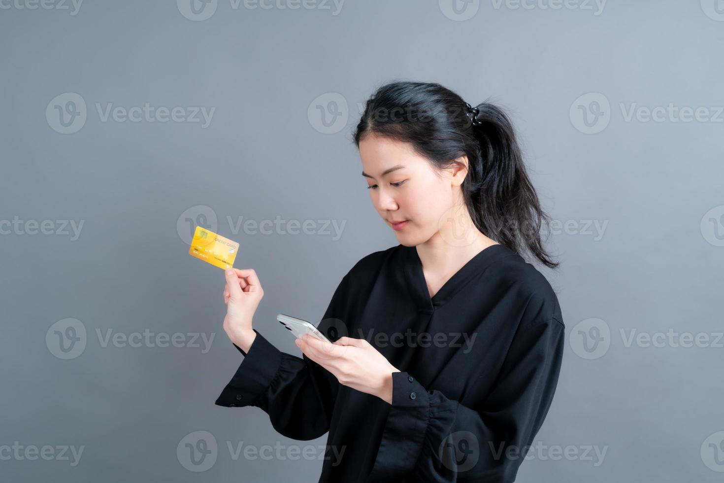 jong Aziatisch meisje dat een plastic creditcard toont terwijl ze een mobiele telefoon vasthoudt foto