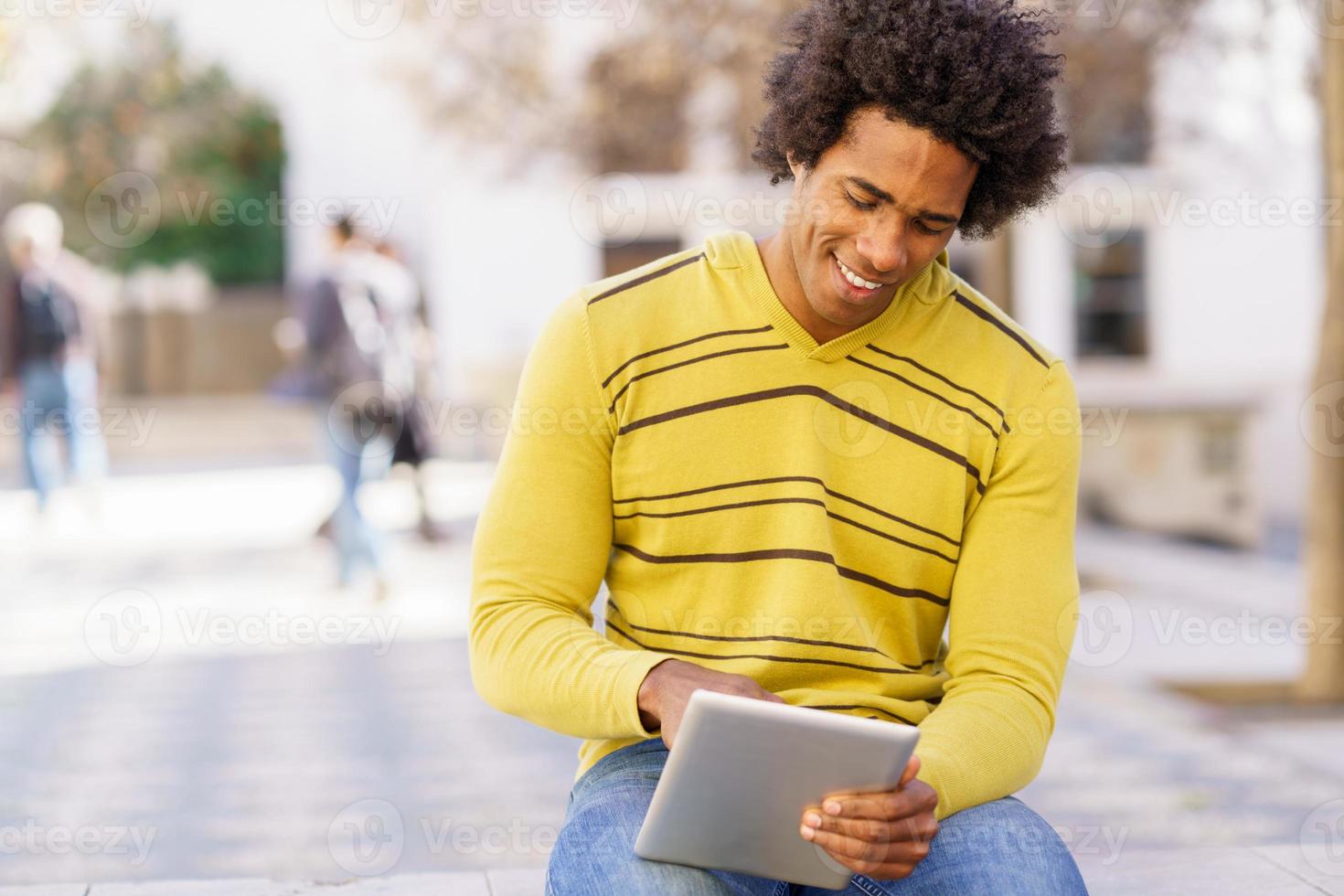 zwarte man met behulp van een digitale tablet zittend op een bankje buiten. foto