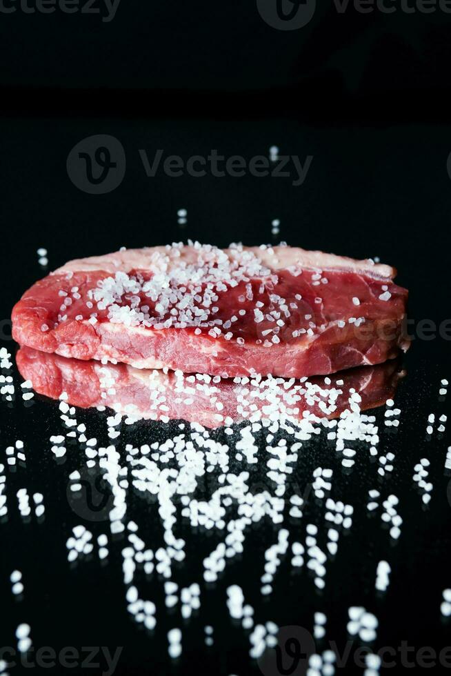 rauw biologisch rundvlees vlees met rozemarijn, kruiden, zout en rood peper Aan zwart achtergrond foto
