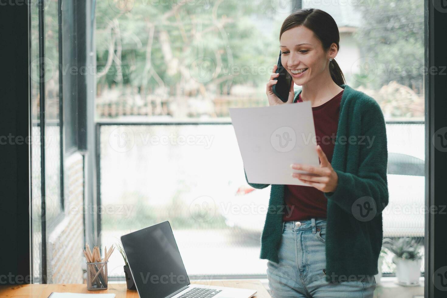 gelukkig zakenvrouw pratend Aan mobiel telefoon terwijl analyseren wekelijks schema in haar notebook. foto