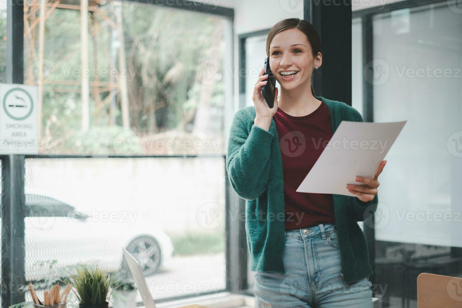 gelukkig zakenvrouw pratend Aan mobiel telefoon terwijl analyseren wekelijks schema in haar notebook. foto