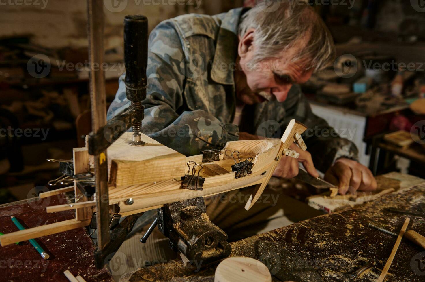 een volwassen timmerman werken Aan een houten speelgoed- zeilboot in zijn werkplaats. vakman maakt handgemaakt houten items foto