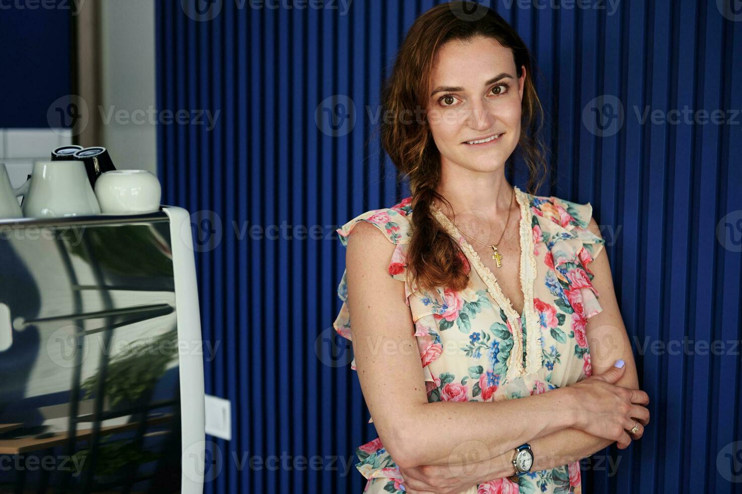 zelfverzekerd portret van een bedrijf vrouw eigenaar van een cafe staand tegen een blauw muur in haar eigen cafe glimlachen terwijl poseren voor de camera foto