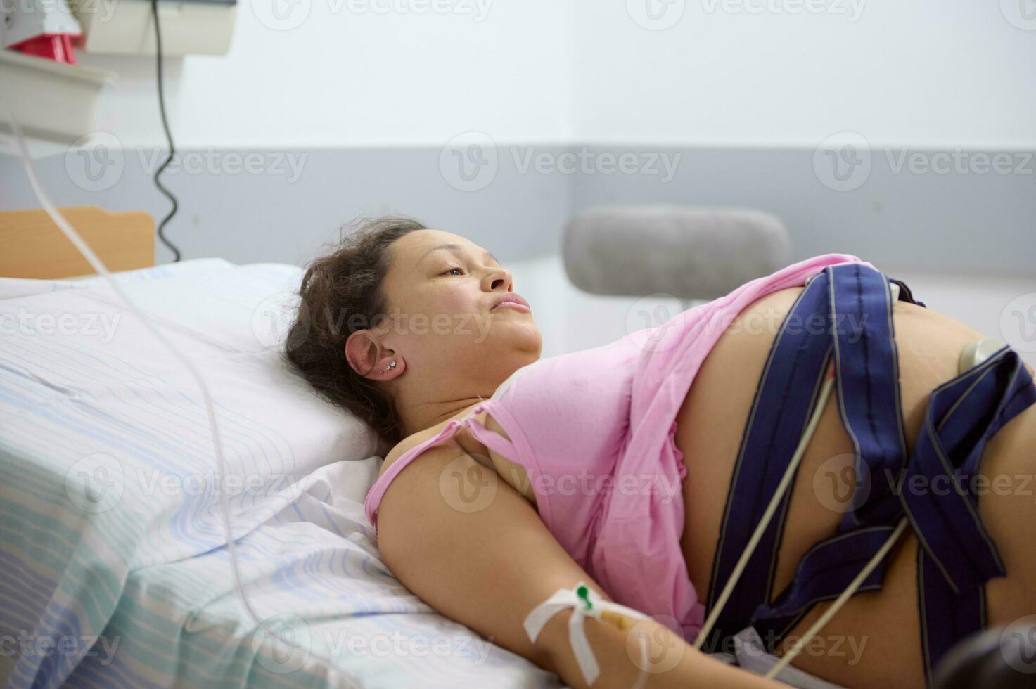 een zwanger vrouw, bevalling moeder in arbeid met een elektrocardiogram cheques haar baby, aan het liegen in ziekenhuis bed. foto