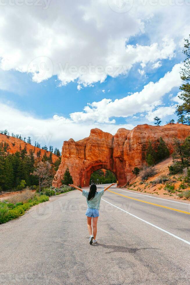 jong gelukkig vrouw in achtergrond van natuurlijk steen boog brug in de rood Ravijn nationaal park in Utah, Verenigde Staten van Amerika foto