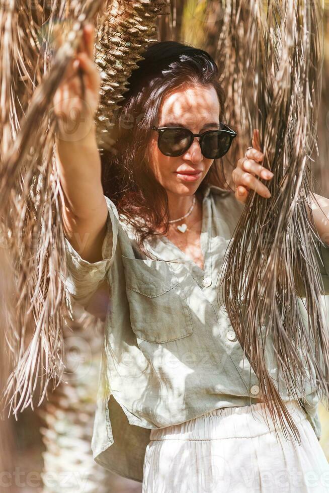 portret van gelukkig jong vrouw buitenshuis tussen palm boom bladeren foto