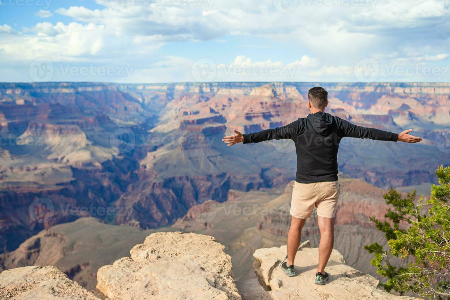 jong wandelaar is staand Aan een steil klif nemen in de verbazingwekkend visie over- beroemd groots Ravijn Aan een mooi zonnig dag, nationaal park, Arizona, Verenigde Staten van Amerika foto
