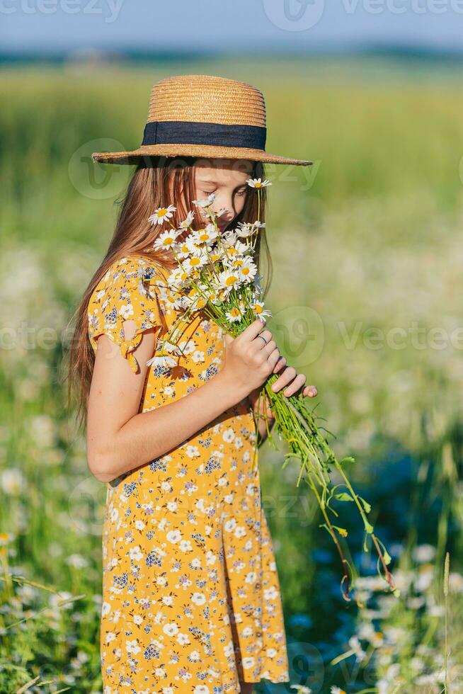 portret van meisje in een geel jurk en rietje hoed Aan een kamille veld- in zomer foto