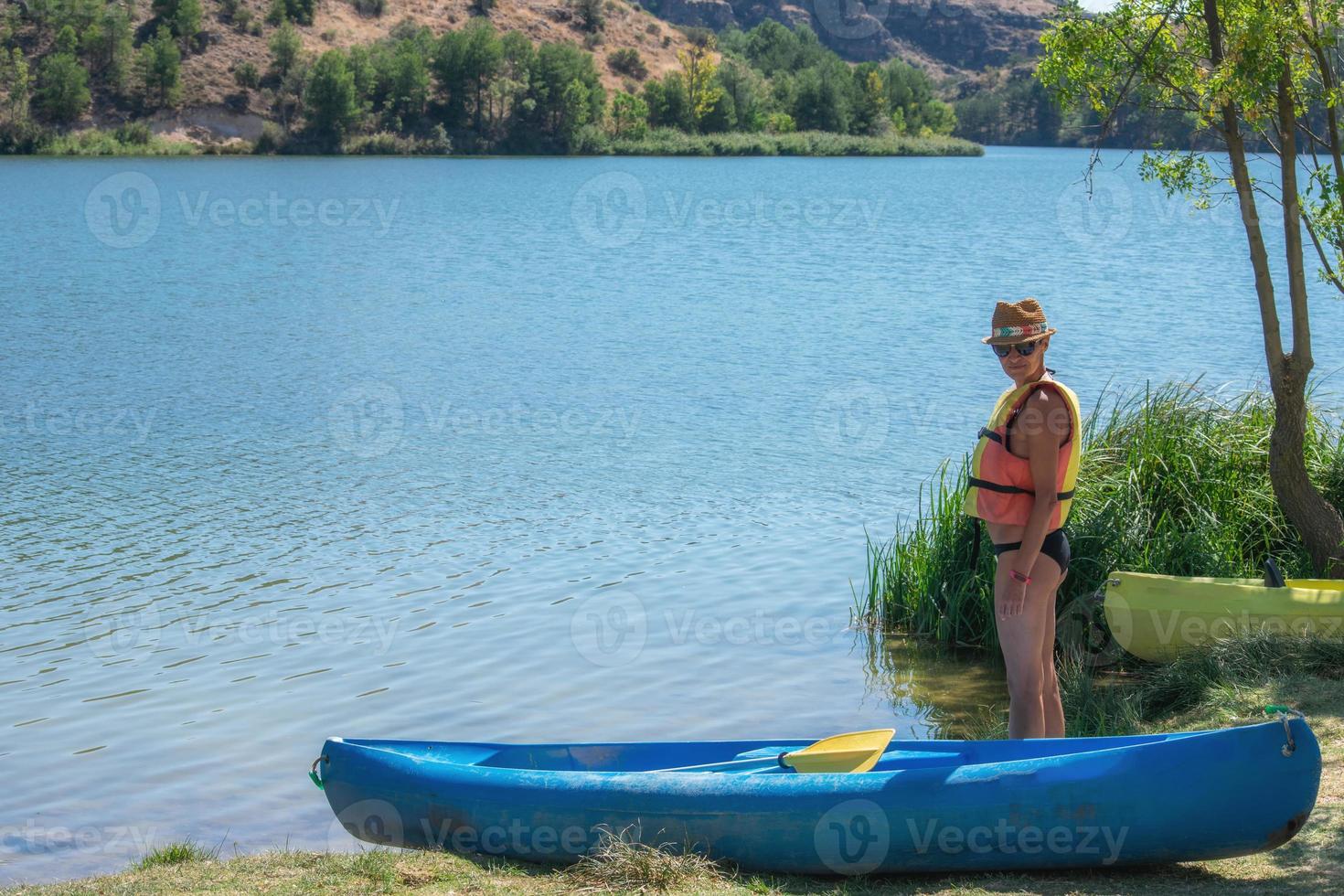 vrouw in een reddingsvest die naast een kano bij het water staat foto