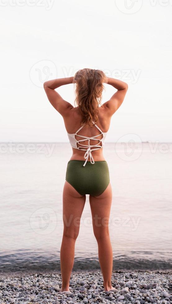 achteraanzicht van een jonge vrouw die op een steenachtig strand staat en naar de zee kijkt foto