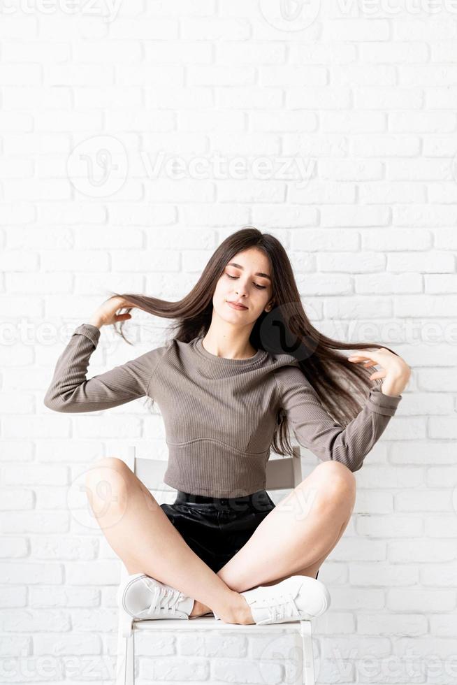 vrouw met lang haar zittend op witte bakstenen muur achtergrond foto