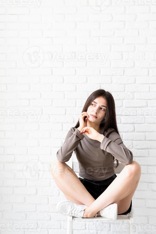 vrouw met lang haar zittend op een witte bakstenen muur achtergrond, denken foto