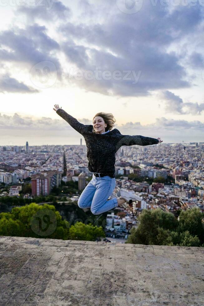 zorgeloos jong vrouw jumping bovenstaand de stad Bij zonsopkomst, Barcelona, Spanje foto