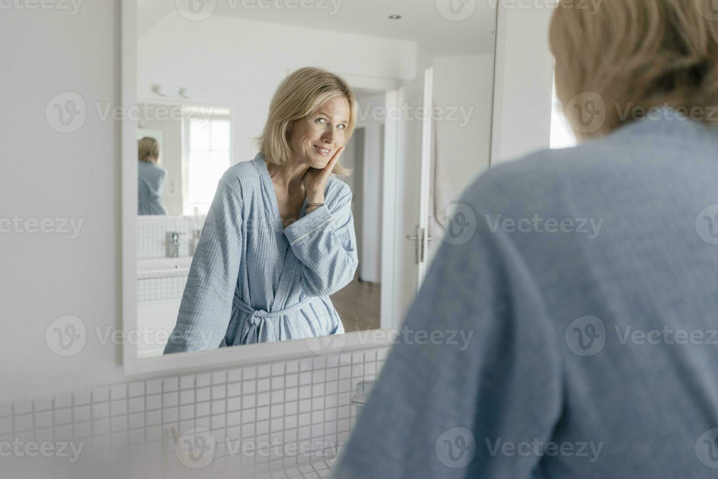 portret van glimlachen volwassen vrouw op zoek in badkamer spiegel foto