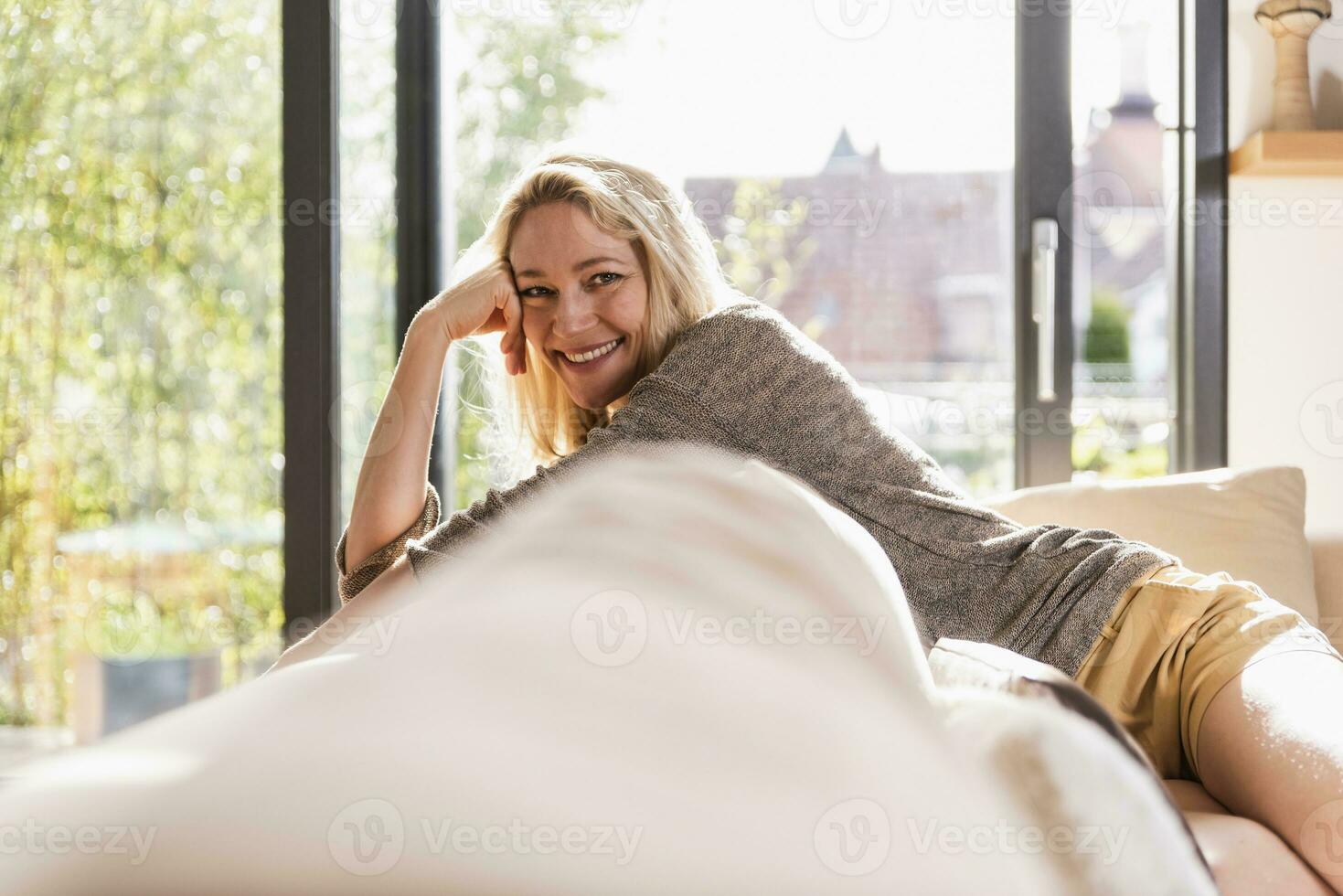 portret van gelukkig volwassen vrouw ontspannende Aan bankstel Bij huis foto