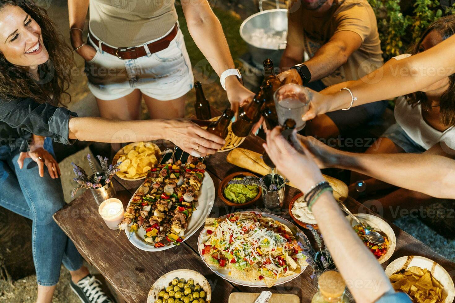 gelukkig vrienden roosteren met bier flessen gedurende een buitenshuis avondeten foto