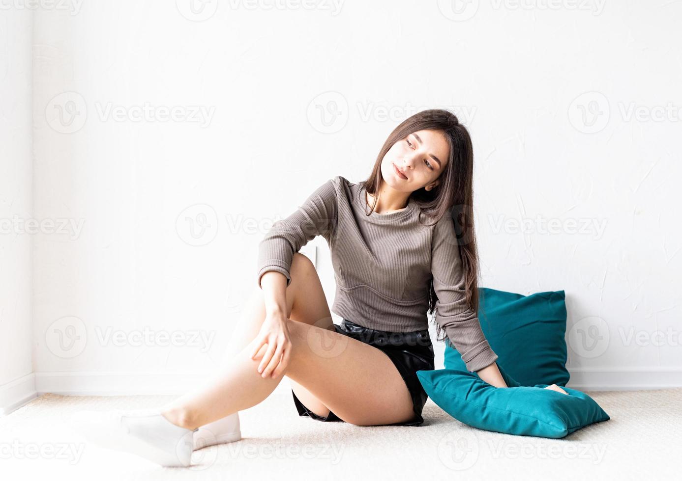 vrouw in vrijetijdskleding zittend op de vloer met kussens glimlachend foto
