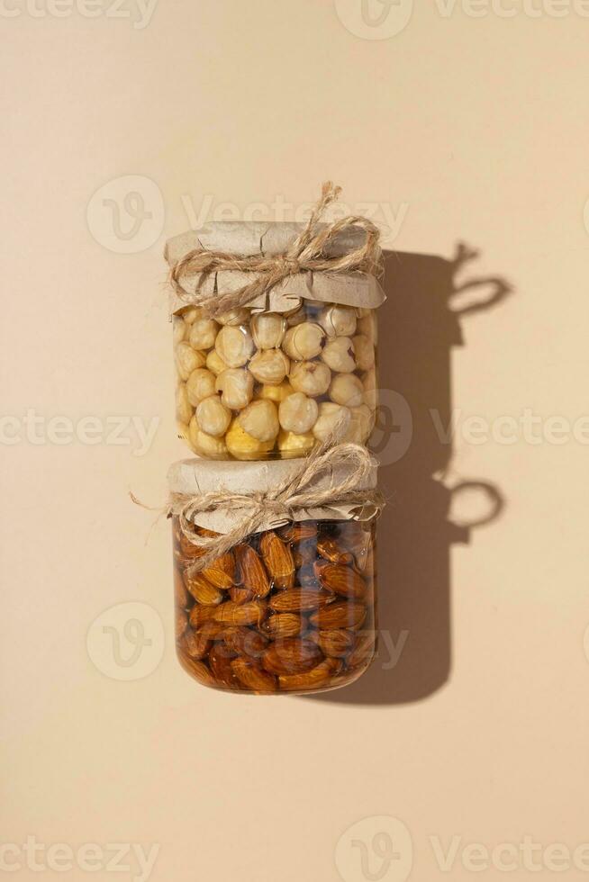 glas potten met noten in honing Aan beige achtergrond top visie met moeilijk schaduwen. foto