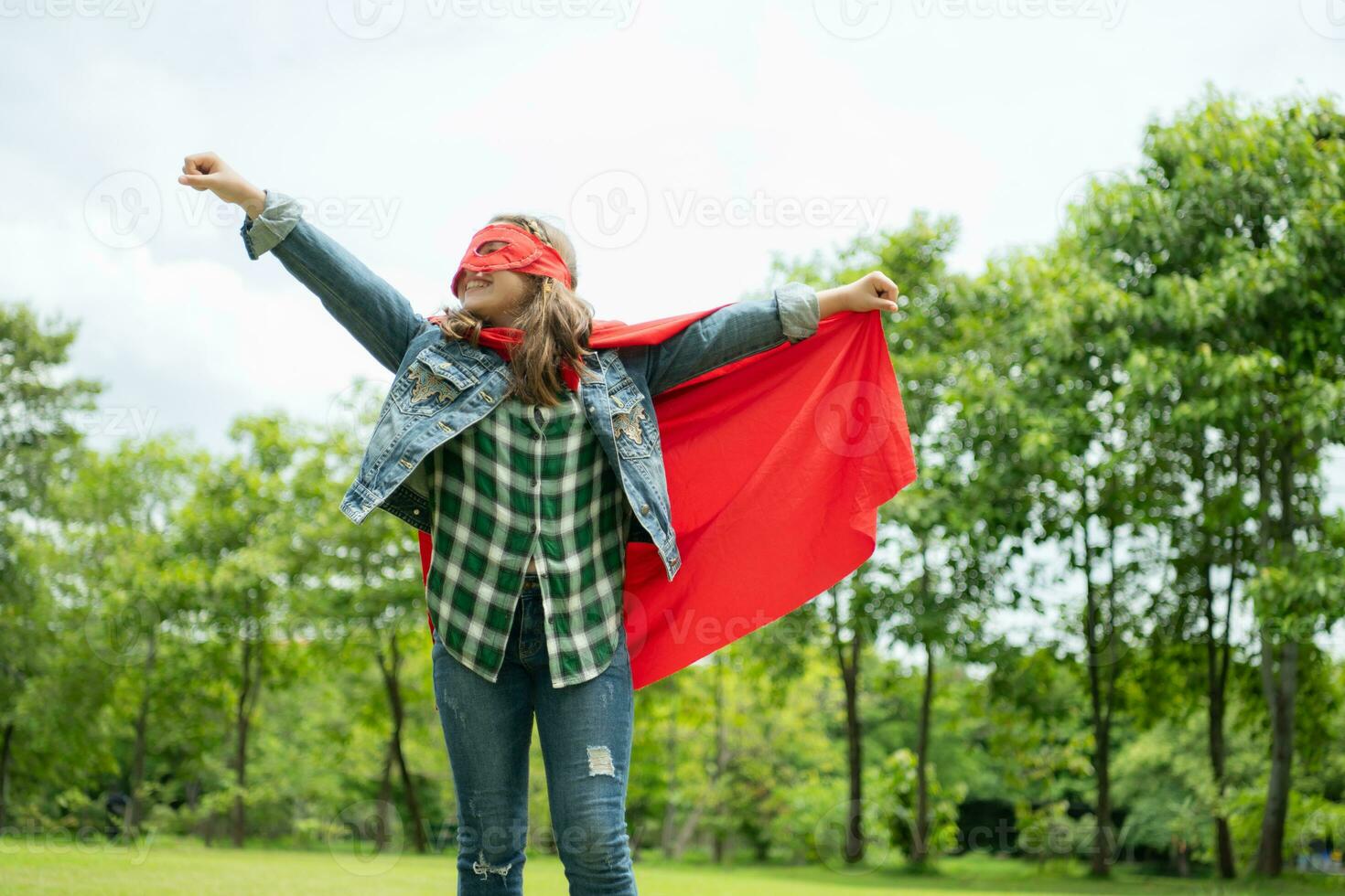 Aan een mooi dag in de park, een jong meisje geniet haar vakantie. speels met een rood superheld kostuum en masker. foto