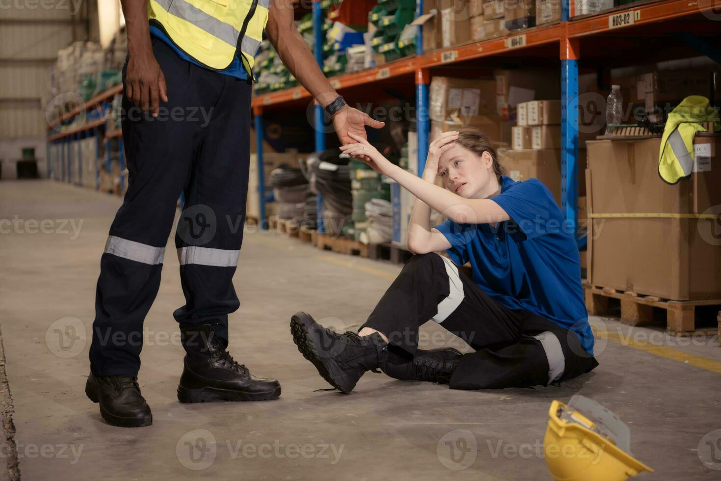 een magazijn arbeider consoles en helpt een vrouw arbeider wie huilt uit in pijn na een been ongeluk in een groot magazijn foto