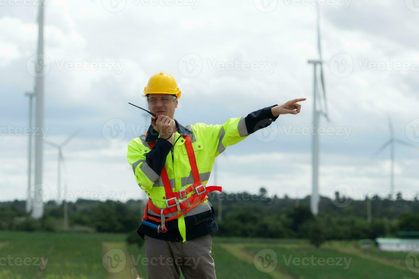 ingenieur in een geel helm en reflecterende hesje Aan de achtergrond van wind turbines gebruik makend van walkie talkie voor communicatie foto