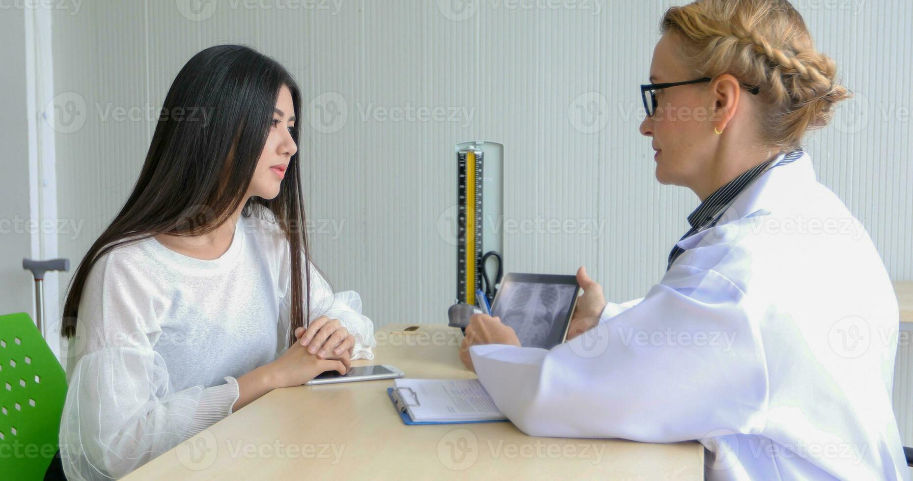 Aziatisch vrouw geduldig zittend met dokter over haar ziekte en tonen röntgenstraal resultaten met bloed druk en hart tarief meting met stethoscoop foto