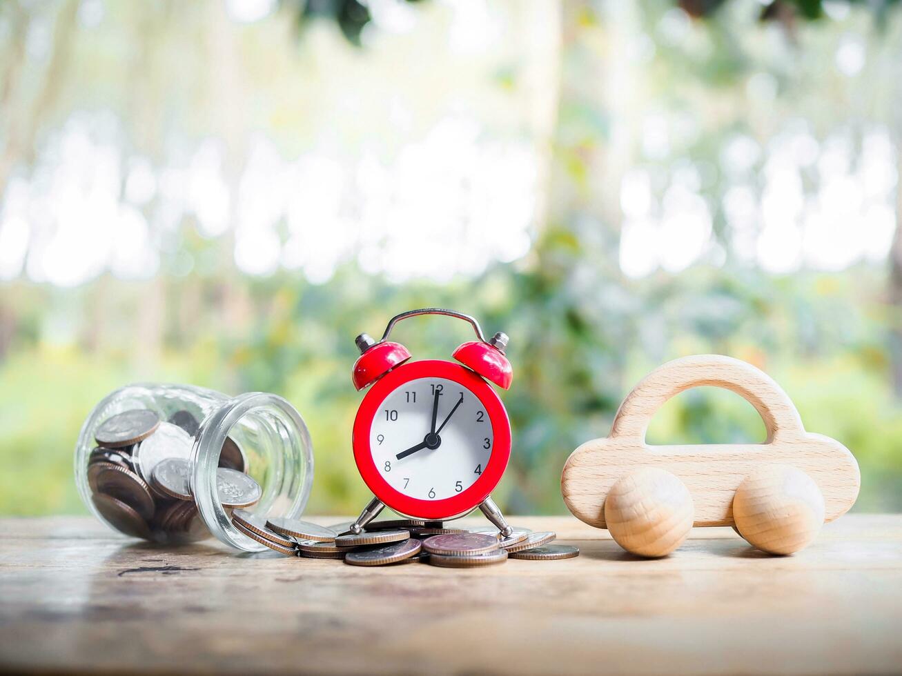 tijd is geld concept. rood alarm en houten speelgoed- auto Aan stack van munten. concept van opslaan geld voor buying een auto in de toekomst. foto