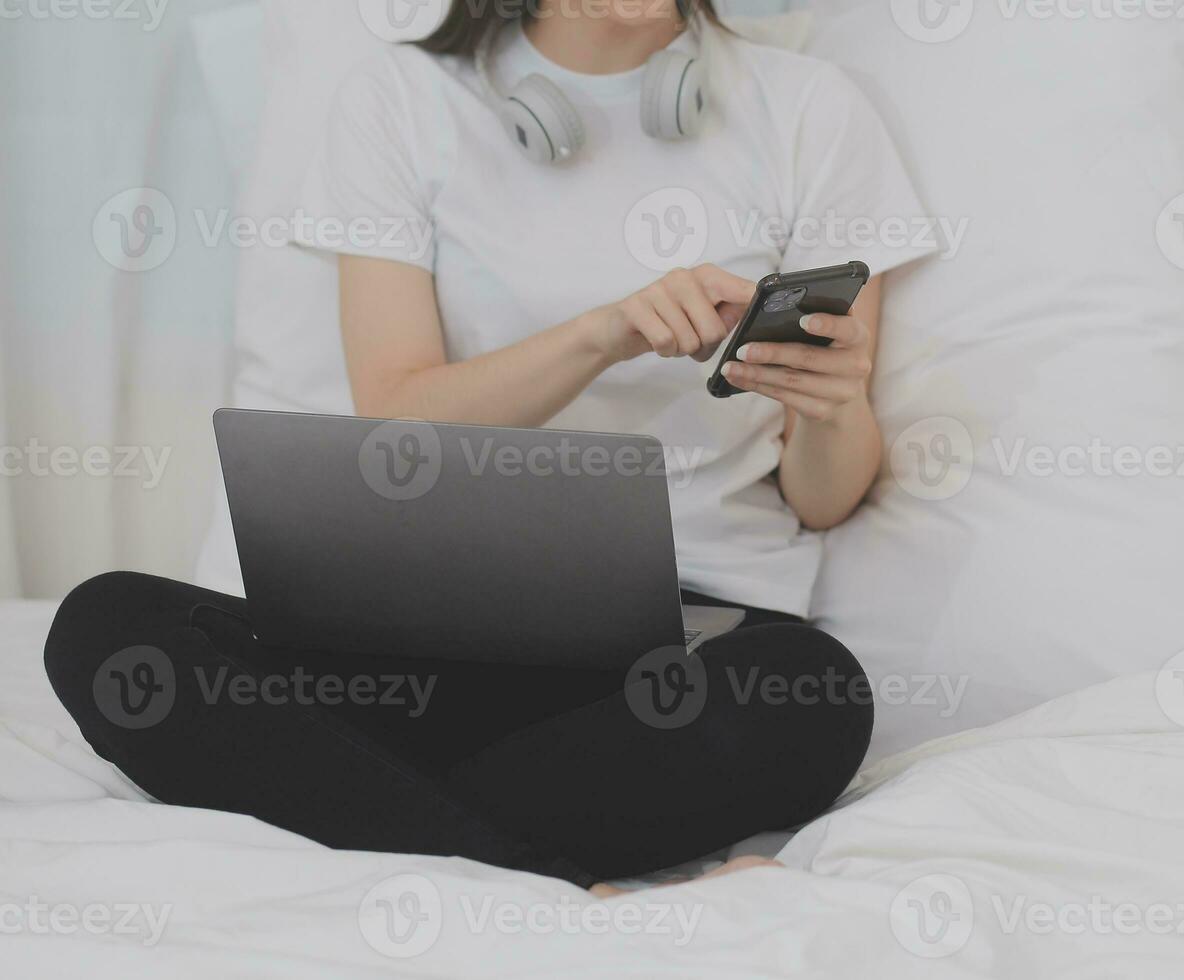 doeltreffend jong millennial meisje zittend Aan een bed in de ochtend, toepassingen laptop computer en eet croissants en drankjes koffie voor ontbijt foto