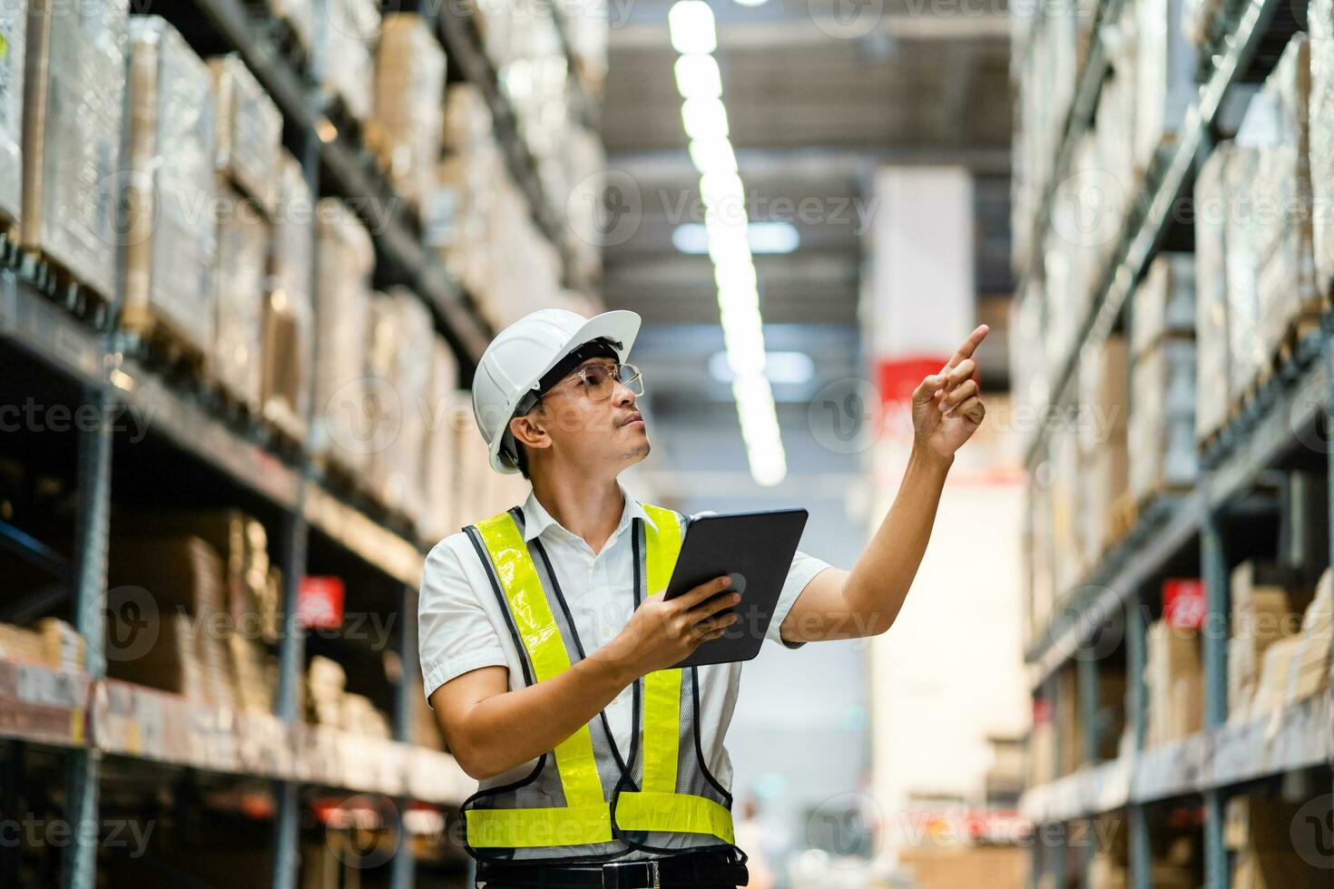 een Aziatisch magazijn manager toepassingen een tablet computer naar inspecteren goederen in een magazijn. logistiek en exporteren bedrijf concept. foto