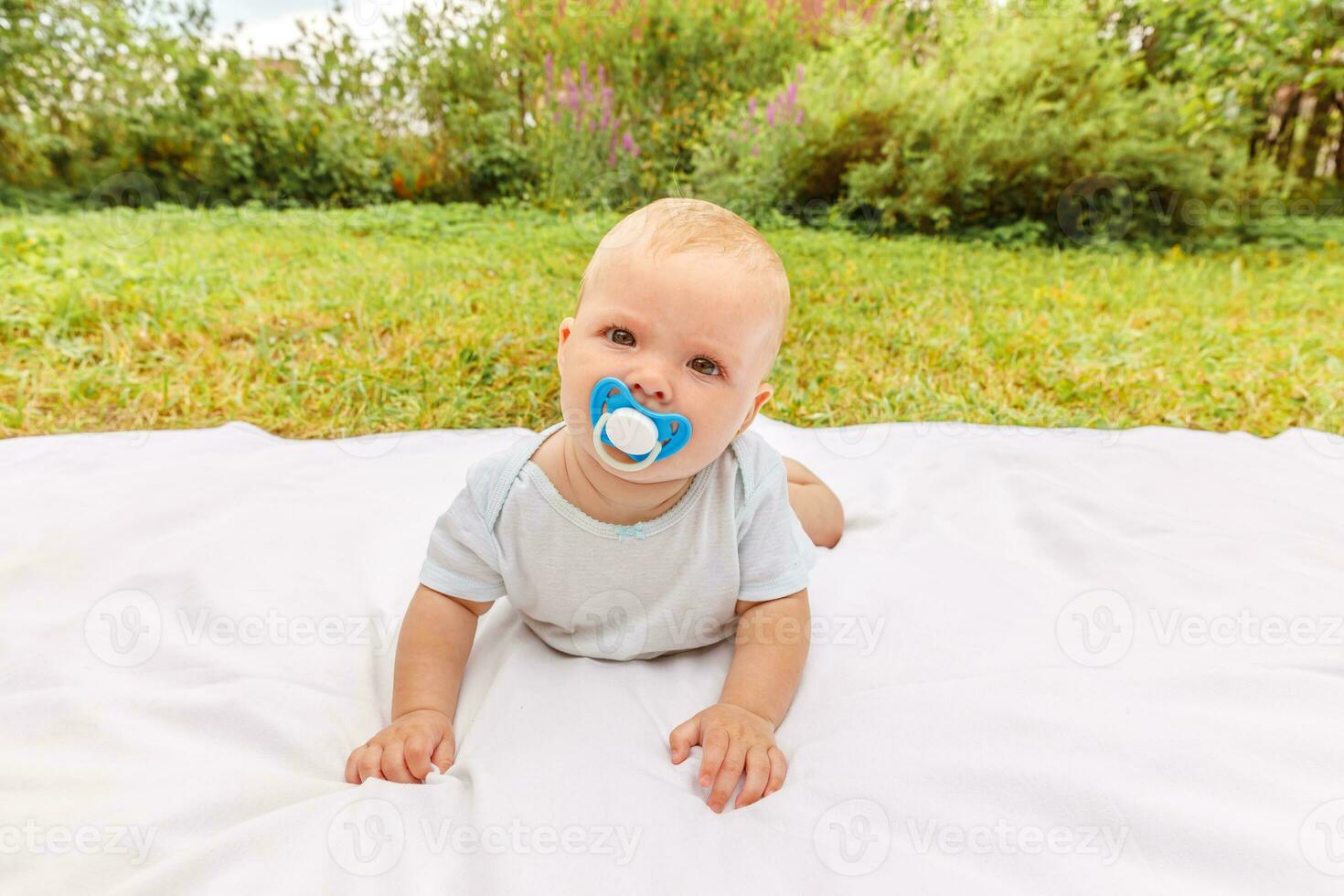 schattig weinig pasgeboren meisje aan het liegen Aan buik Aan deken in gazon Aan zonnig zomer dag buitenshuis. zuigeling hebben pret buitenshuis. zuigeling baby kind resting spelen aan het leren naar kruipen. moederschap gelukkig kind concept. foto