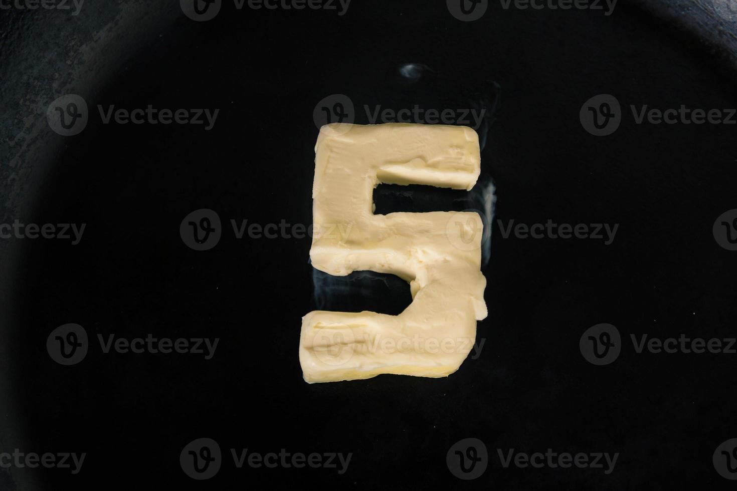 boter in de vorm van nummer 5 op hete pan - close-up bovenaanzicht foto