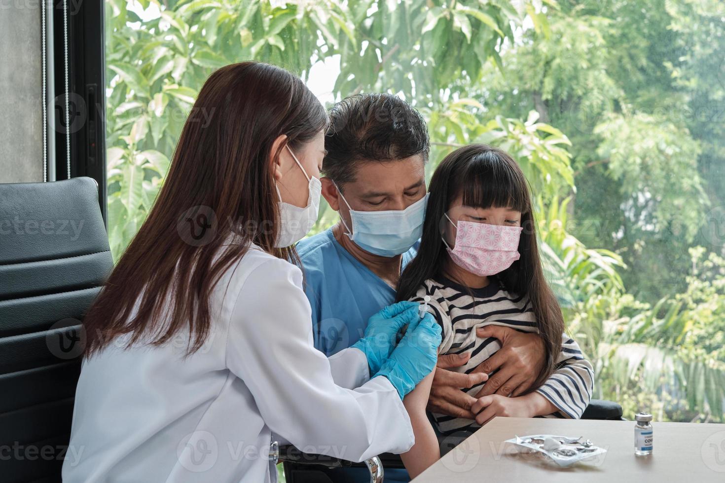 vrouwelijke arts die Aziatisch meisje vaccineert bij de kinderkliniek. foto
