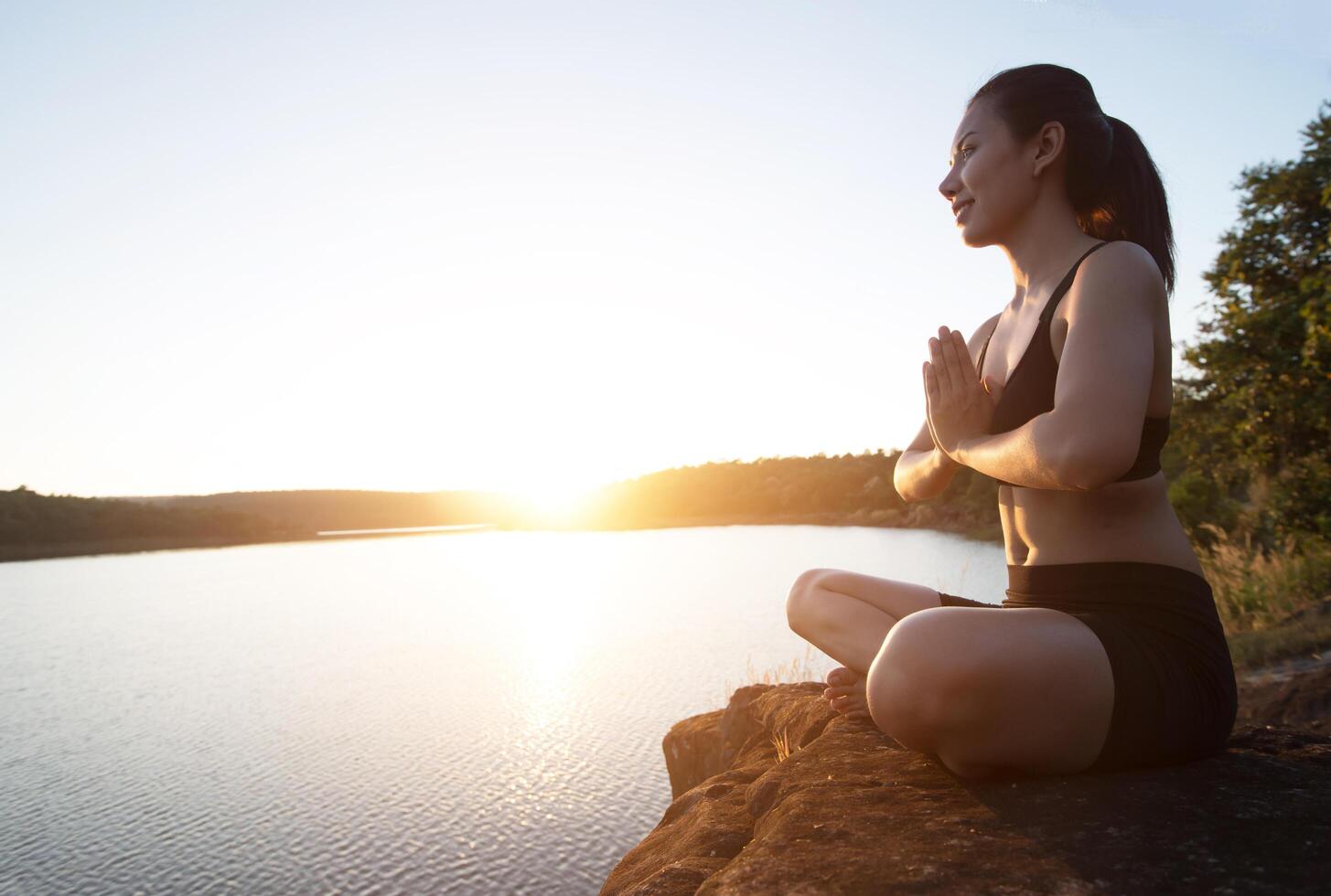 jonge gezonde vrouw beoefent yoga bij bergmeer tijdens zonsondergang. foto