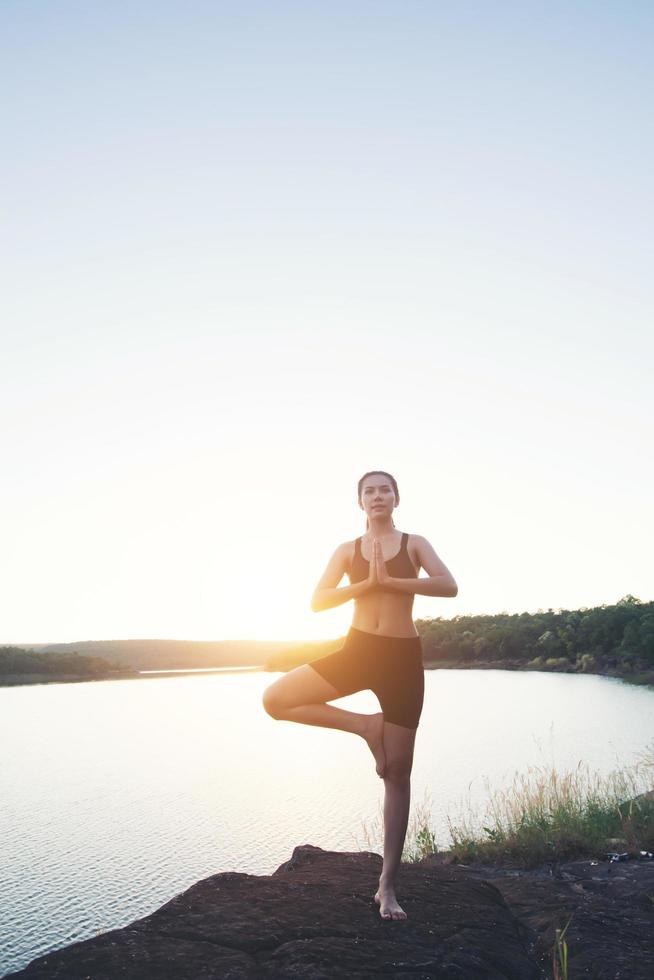 jonge gezonde vrouw beoefent yoga bij bergmeer tijdens zonsondergang. foto