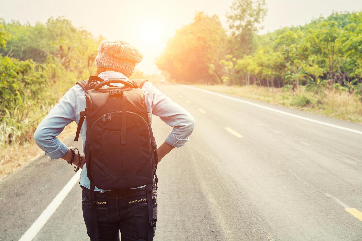 jonge vrouw liftend met rugzak zittend op de weg foto