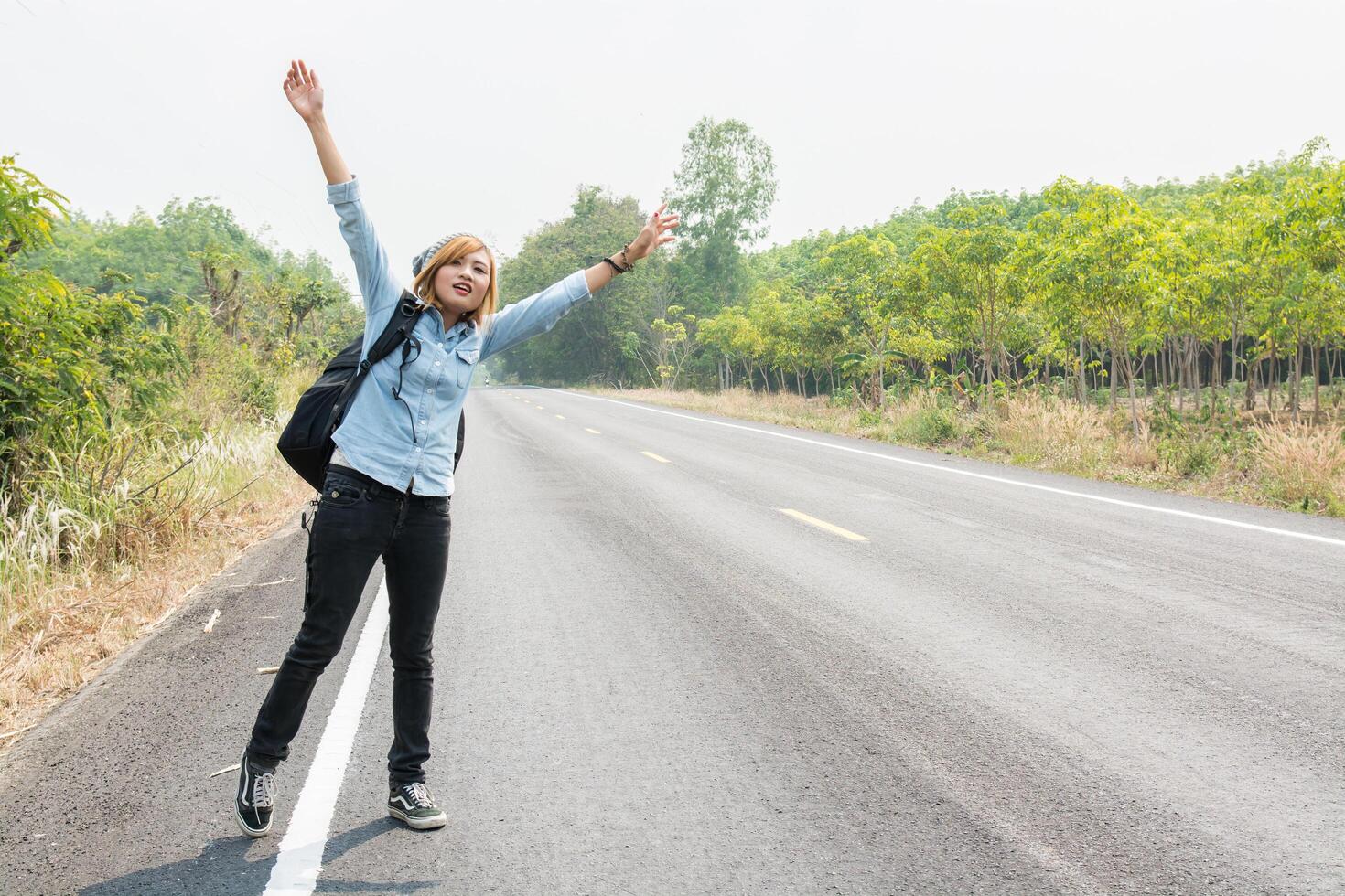 hipster vrouw liftend op landelijke weg op zoek naar de auto foto