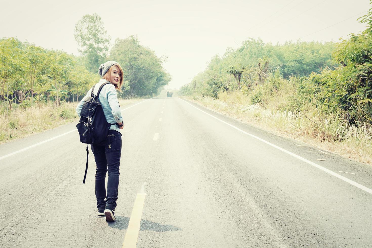 jonge vrouw liftend met rugzak zittend op de weg foto