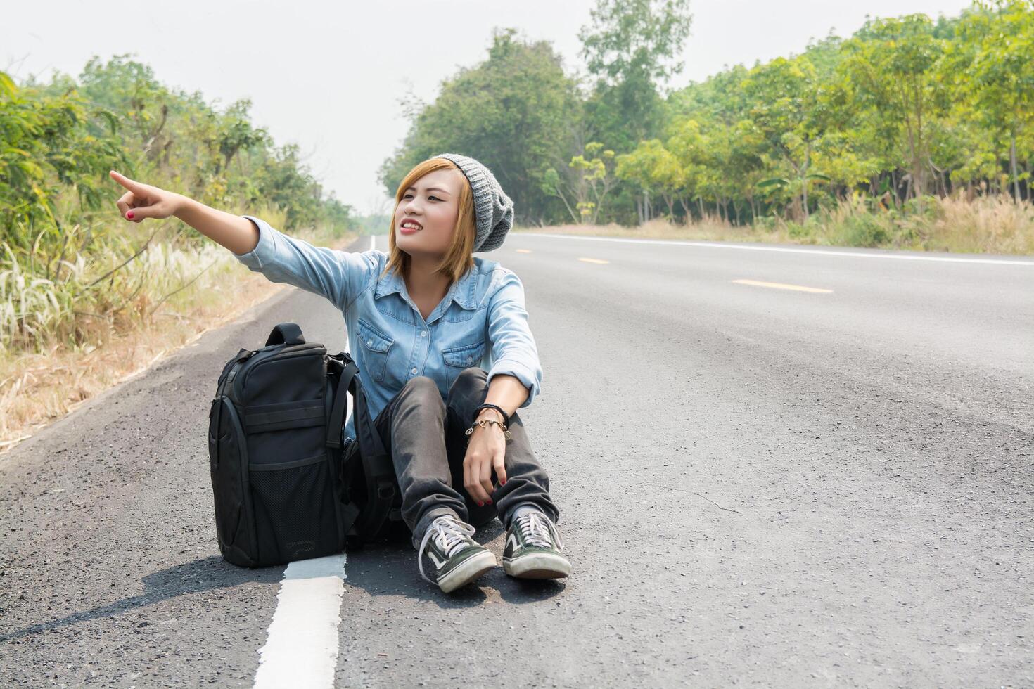 jonge vrouw liftend met rugzak zittend op de weg foto