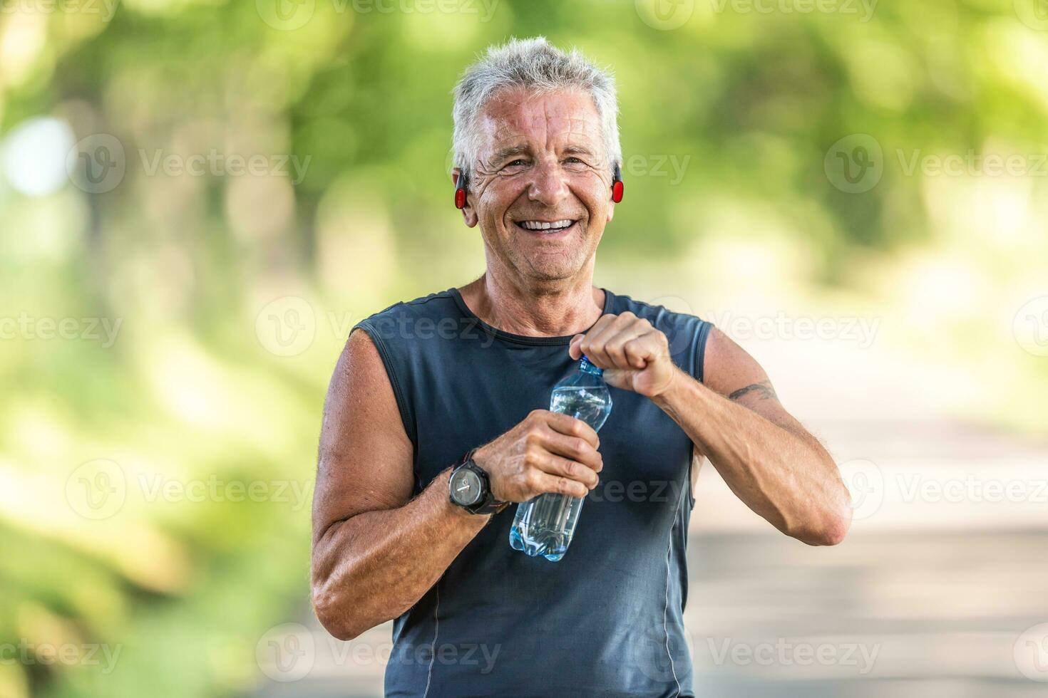 lachend, fit en gepensioneerd Mens met grijs haar- glimlacht net zo hij opent omhoog een fles van water na afwerking een aëroob training foto