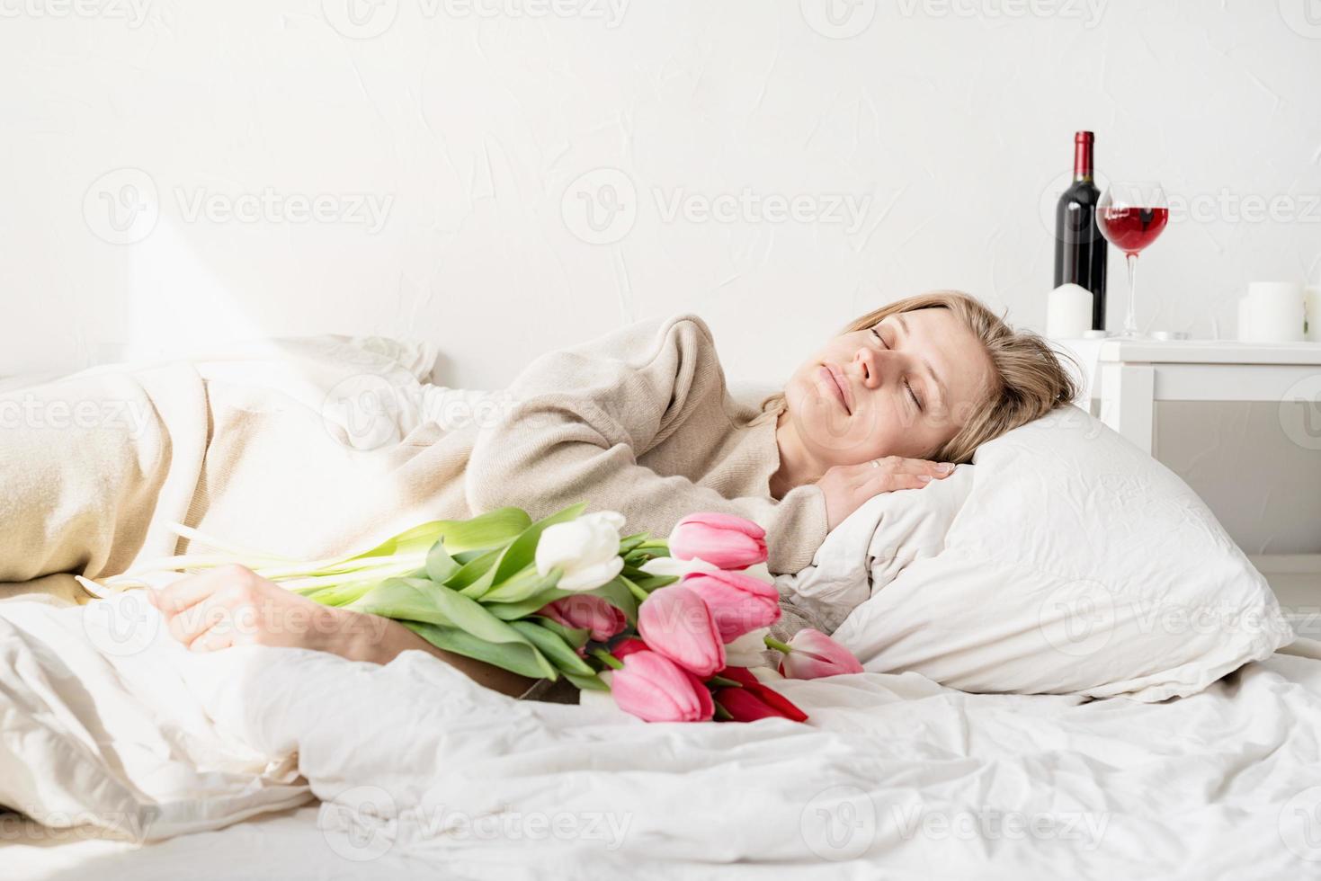 vrouw die in het bed ligt en een pyjama draagt met een boeket van tulpenbloemen foto