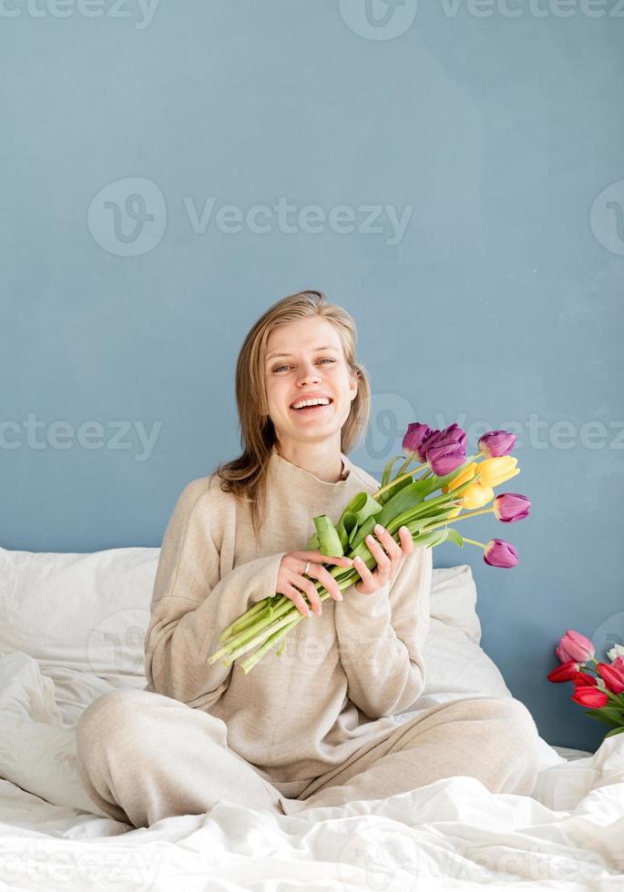 vrouw zittend op het bed met tulp bloemen boeket foto