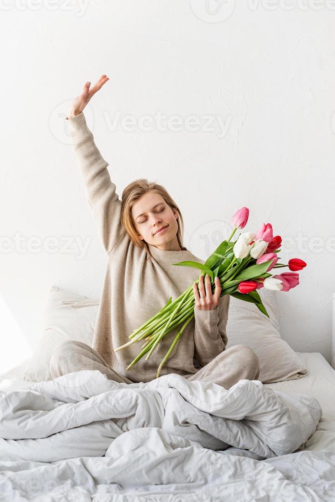vrouw zittend op het bed met een pyjama aan die zich uitstrekt foto