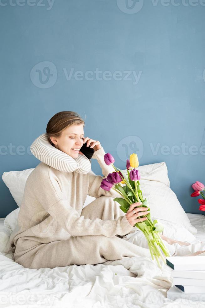 gelukkige vrouw die op het bed zit en een pyjama draagt die aan de telefoon praat foto