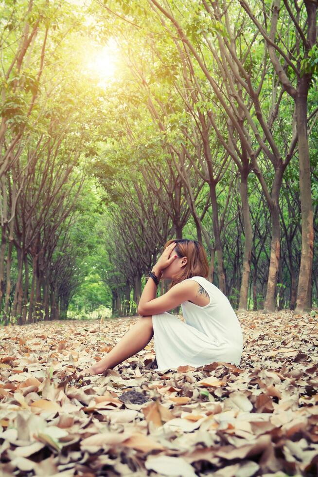 trieste vrouw handen van haar gezicht af, zo droevig zittend op droog blad. foto